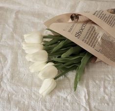 white tulips are laid out on a bed with a paper bag and tag