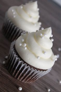 two cupcakes with white frosting and sprinkles on a table