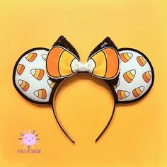 an orange and black mickey mouse ears with candy corn on it's ears, against a yellow background