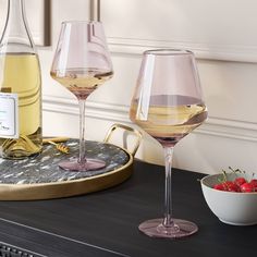 two wine glasses on a table with a bowl of strawberries and a bottle of wine