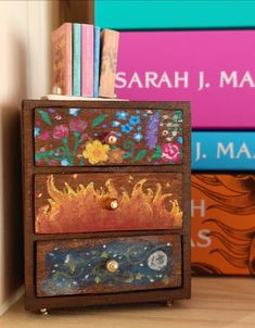 three drawers with books on top of them and some flowers painted on the bottom one