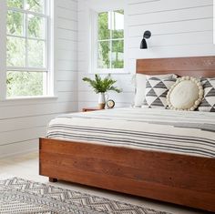 a bedroom with white walls and wooden bed frame, striped pillows, and rugs