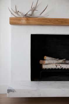 a white fireplace with logs in it and antlers on the mantle