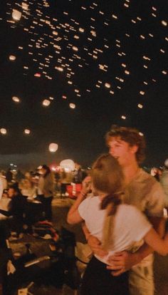 two people are hugging each other in front of the sky full of lights at night