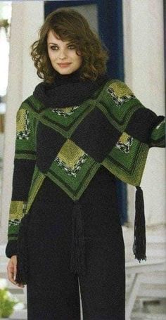 a woman standing in front of a building wearing a green and black sweater with tassels