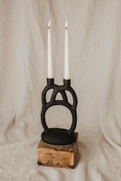 two white candles sitting on top of a piece of wood next to a black candle holder