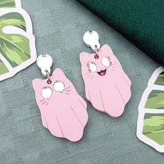 Spooky Kitty earrings are fun for any time of the year. Current colorways include Void (black with purple eyes), Light (white with light blue eyes), Spring (pastel green with pink eyes), or Blush (pink with silver eyes). They are made with mirror and matte acrylics and engraved with details. A cute accessory for any aesthetic. Get them with default studs as pictured, or if you select fishhooks, huggies/leverbacks, or clip-ons the teardrop on top will be replaced. If you would like gold-toned met Matte Acrylics, Toothpaste Kisses, Spooky Kitty, Laser Jewelry, Silver Eyes, Light Blue Eyes, Earring Inspo, Ears Pierced, Weird Jewelry