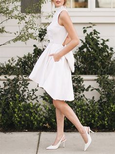 a woman in a white dress is walking down the street with her hand on her hip