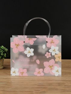 a pink and white flower bag sitting on top of a wooden table next to a potted plant