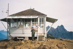 two men standing in front of a small white building on top of a rocky hill