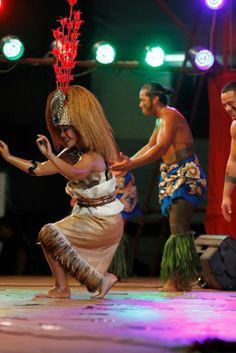 some people are dancing on a stage with lights in the background and one woman is wearing a headdress