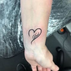 a woman's arm with a small heart tattoo on her left wrist and the word dad written in cursive font