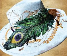 Elevate your hat accessory game with this stunning hand-painted tooled leather feather inspired by the vibrant hues of a peacock feather. Crafted with care, this lightweight, durable leather feather is a versatile piece that can be used on any hat. The intricate details of the feather capture the iridescent gold, greens, and purples, making it a perfect addition to your Mardi Gras bohemian or festival style or as a thoughtful Krewe gift for a king and queen or just someone special. Key Features: *Material: Genuine leather, painted and tooled by hand *Design: Vibrant peacock feather with metallic accents *Uses: hat band or charm *Size: Approximately 12 inches *Lightweight and durable *Perfect for: Mardi Gras bohemian festival krewe gifts King Queen holidays weddings or everyday gifts Why Yo Peacock Hat, Peacock Feather Art, Hand Design, Boho Feathers, Feather Hat, Feather Art, Bohemian Festival, Hand Painted Leather, Everyday Gifts