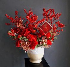 a white vase filled with red flowers on top of a black table next to a gray wall