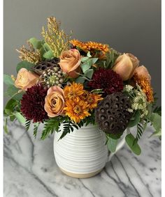 a white vase filled with lots of flowers on top of a marble countertop next to a wall