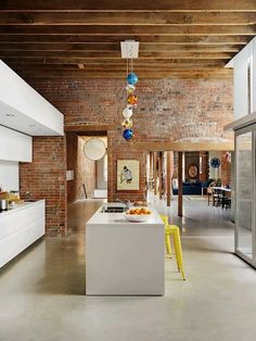 an open kitchen and dining room with exposed brick walls, white cabinets and yellow chairs