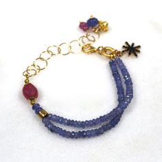 Glittering, vibrantly hued genuine polished natural periwinkle hued tanzanite, one of the rarest and most prized of all gemstones, sparkles on this strand in a beautiful bright striking splash of color! A plump faceted pink sapphire accents the side of the wrist. 14k gold fill chain and colorful drop embellishments add a little chic bling. l Blue Faceted Amethyst Jewelry, Faceted Blue Amethyst Jewelry, Tanzanite Gemstone Bracelet Jewelry, Blue Tanzanite Bracelet Jewelry, Blue Amethyst Bracelets With Natural Stones, Blue Tanzanite Bracelet, Blue Tanzanite Gemstone Bracelets, Blue Amethyst Beaded Bracelets As Gift, Blue Amethyst Beaded Bracelets For Gift