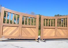 two large wooden gates are shown in front of some bushes and trees on the other side