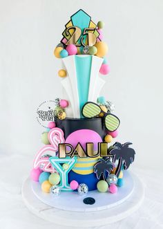 a cake decorated with balloons and other items on a white tableclothed surface in front of a white backdrop