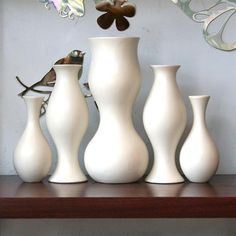 four white vases sitting on top of a wooden shelf