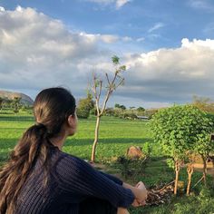 a woman sitting on a bench looking at a giraffe in an open field