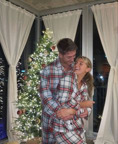 a man and woman standing in front of a christmas tree with their arms around each other