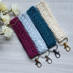 four crocheted key fobs are lined up on a table next to flowers