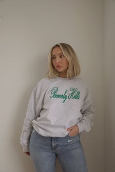 This sweatshirt has a green cursive Beverly Hills graphic on the front. It is made from a soft cotton blend, making it perfect for lounging or running errands in style. Additionally, the sweatshirt is fleece lined for added comfort. embroidered beverly hills ash grey fleece lined crew neck oversized true to size model is wearing a s/m. Height is 5'4", Bust is 33", Waist 28", and Hips 42" wearing sizes 6-8. Spring Cotton Sweatshirt With Lettering, Trendy College Sweatshirt With Embroidered Text, Comfy Green Sweatshirt For Spring, Green Relaxed Fit Cozy Sweats, Cozy Green Relaxed Fit Sweats, Relaxed Fit Lettering Sweatshirt For Spring, Fall Sweatshirt With Embroidered Logo For Loungewear, Spring Lettering Sweatshirt Relaxed Fit, Relaxed Fit Sweatshirt With Lettering For Spring