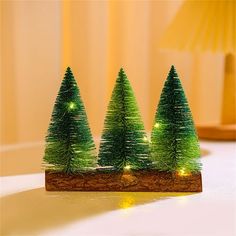 three small christmas trees sitting on top of a wooden table next to a lamp in a room