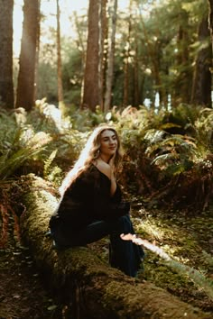 a woman is sitting on a log in the woods