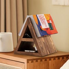 a wooden triangle shaped book stand with books on it next to a coffee cup and radio