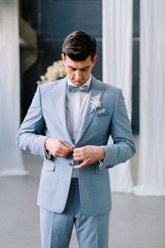 a man in a blue suit adjusts his bow tie