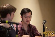 two young men sitting at a table with microphones in front of them and one is looking down