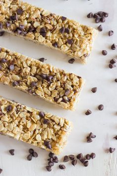 three granola bars are lined up on a white surface with chocolate chips scattered around them