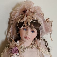 a doll wearing a pink dress and bonnet with flowers on it's head is posed against a white wall