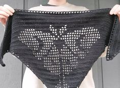 a woman holding up a crocheted triangle shawl