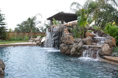 an outdoor pool with waterfall and rocks in the middle, surrounded by greenery on either side