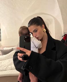 a woman holding a baby taking a selfie in front of her mirror with an iphone