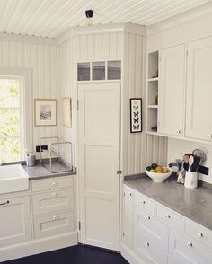 a kitchen with white cabinets and gray counter tops, along with a bowl of fruit on the counter