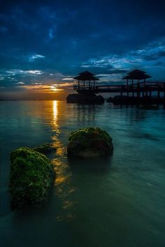 the sun is setting over some rocks in the water