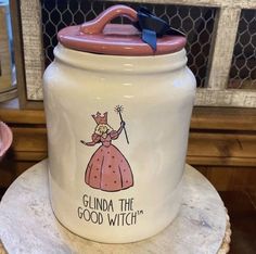 a white cookie jar sitting on top of a wooden table next to a pink cup