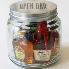 a glass jar filled with liquor bottles on top of a white table next to an open bar sign