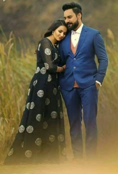 a man and woman standing next to each other in front of tall grass with trees