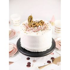 a white cake with gold letters and sprinkles on it sitting on a black plate