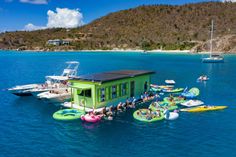 people are floating on inflatable rafts near a small green house with a black roof