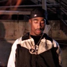 a young man wearing a black hat and jacket standing in front of some stairs with his eyes closed