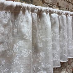 the curtain is hanging on the brick wall by it's side, with white flowers and leaves