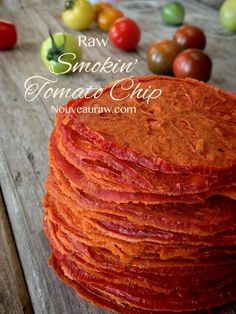 a stack of raw smoked tomato chips on a wooden table with tomatoes in the background