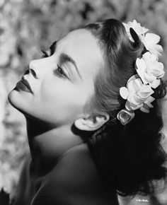 a black and white photo of a woman with flowers in her hair, looking off to the side