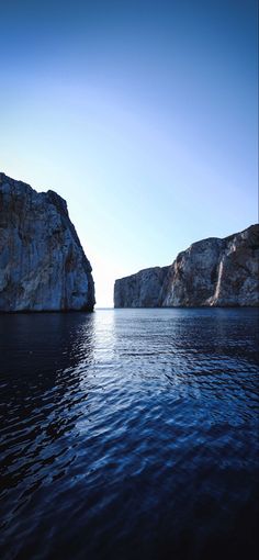 the water is calm and blue with rocks in the background